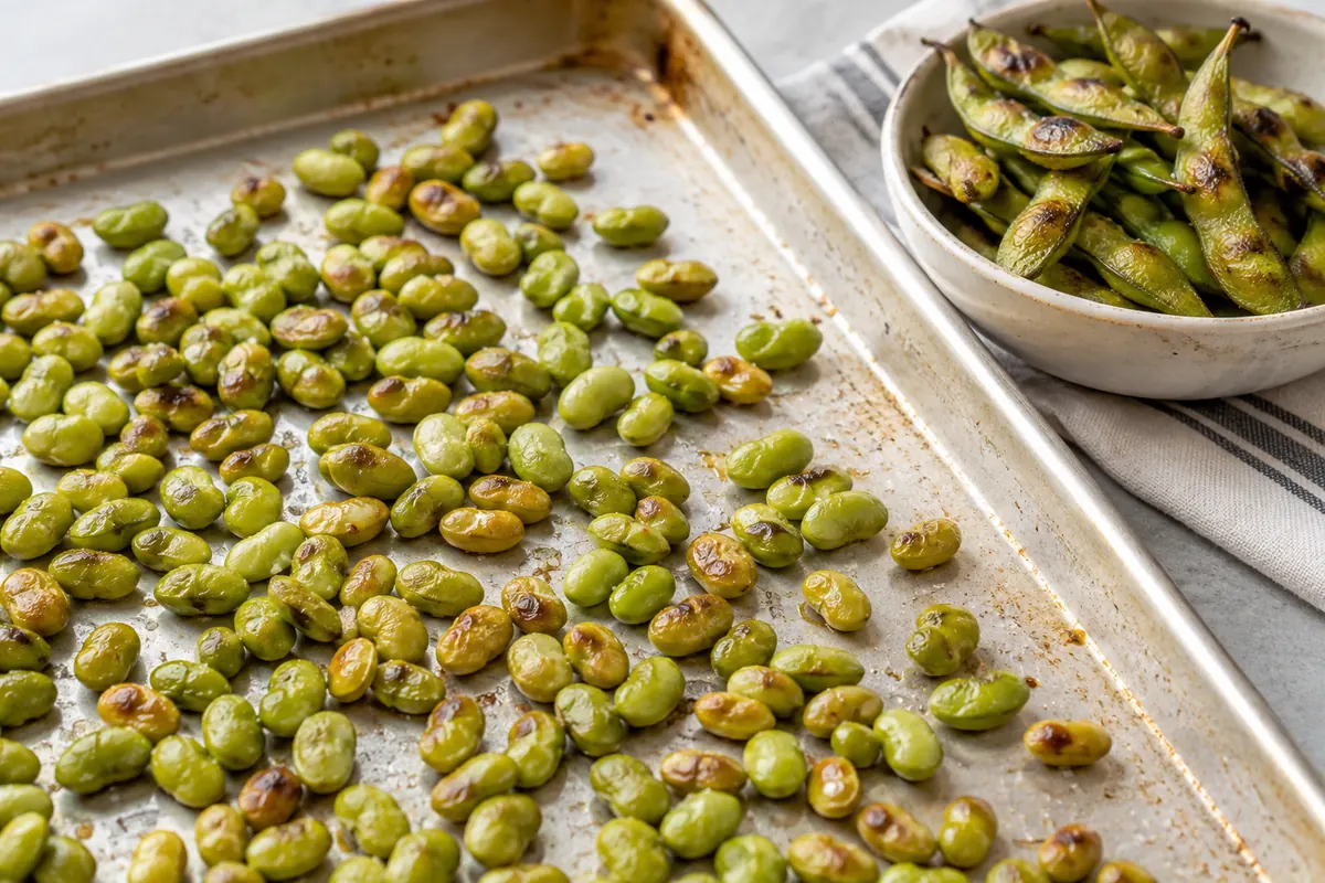 Roasted shelled edamame on a tray beside roasted pods